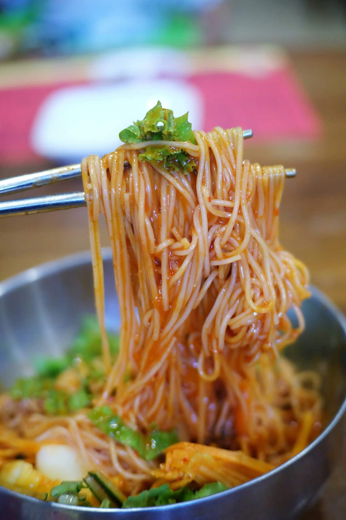 Spicy red-sauced noodles lifted with chopsticks over a metal bowl
