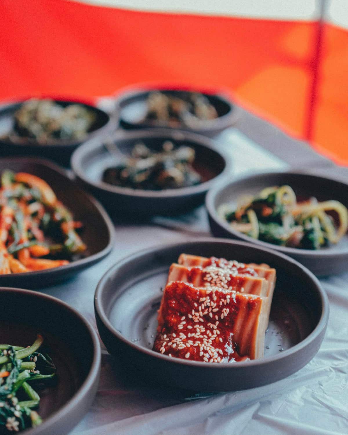 Sliced tofu topped with gochujang sauce next to seasoned banchan