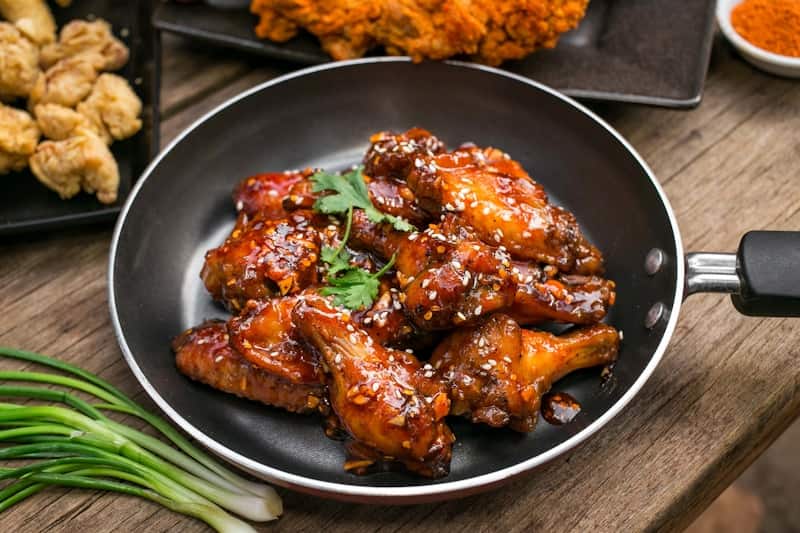 Glossy soy garlic glazed fried chicken wings garnished with sesame seeds in a pan