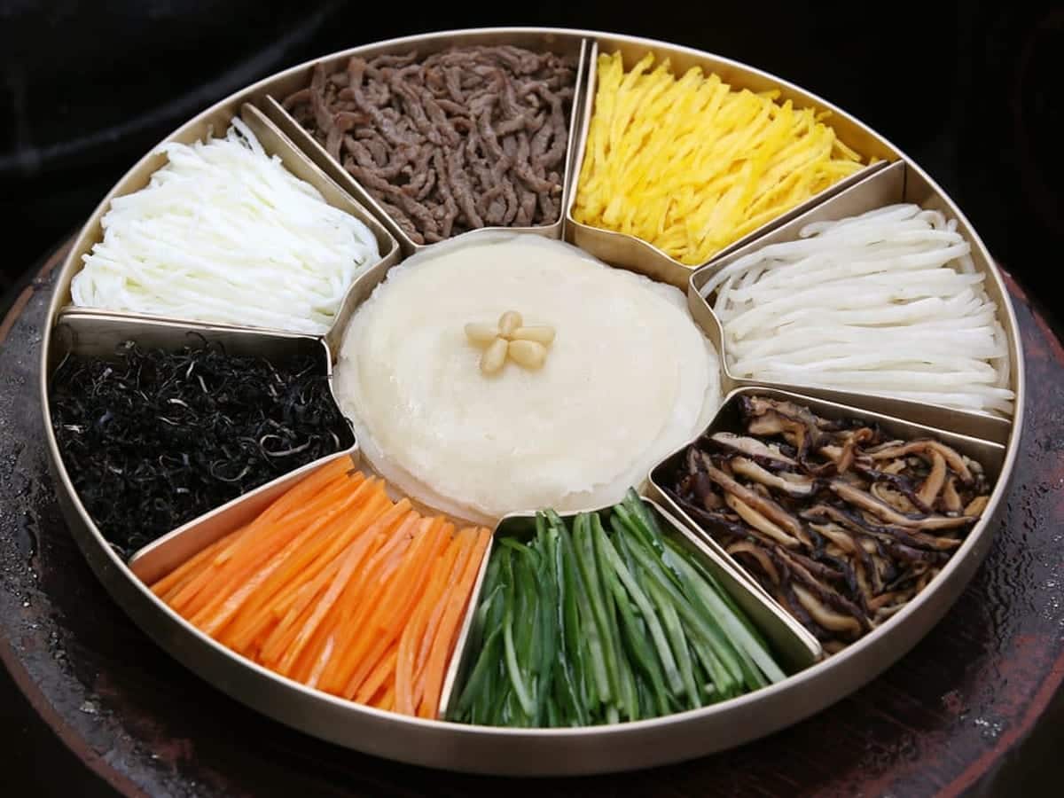 A round platter divided into nine sections filled with vegetables, egg and crepes