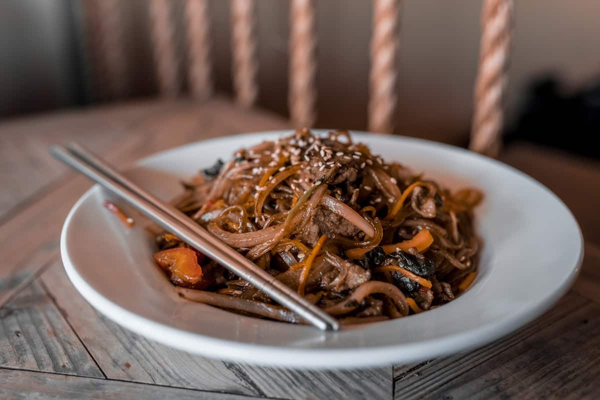 Japchae glass noodles with beef, carrots, and sesame seeds on a white plate