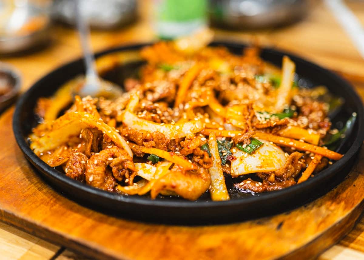 Spicy stir-fried pork with onion and carrot on a sizzling plate