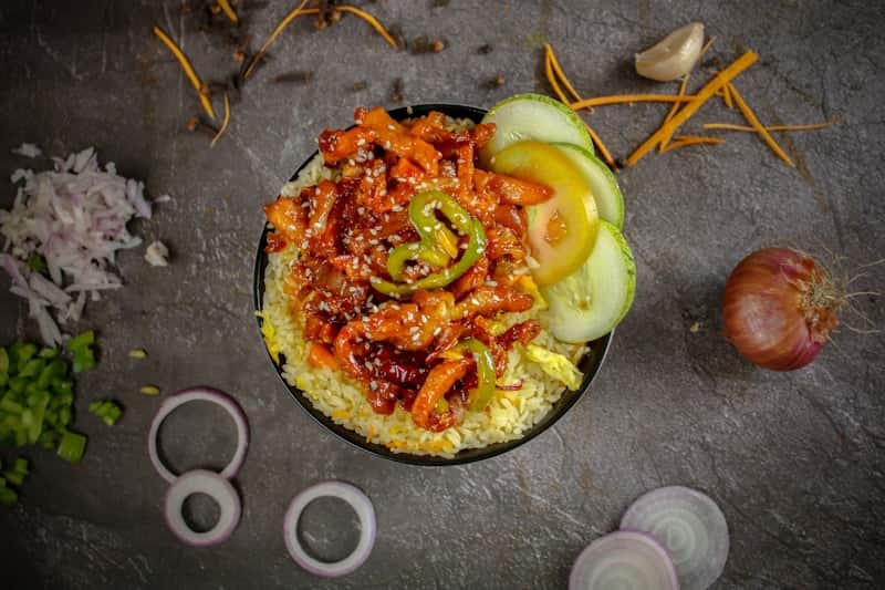 Spicy stir-fried pork over rice with cucumber slices in a black bowl