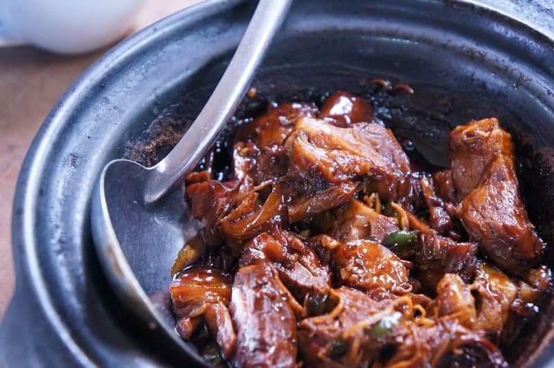 Glossy dark braised short ribs in a clay pot with a ladle