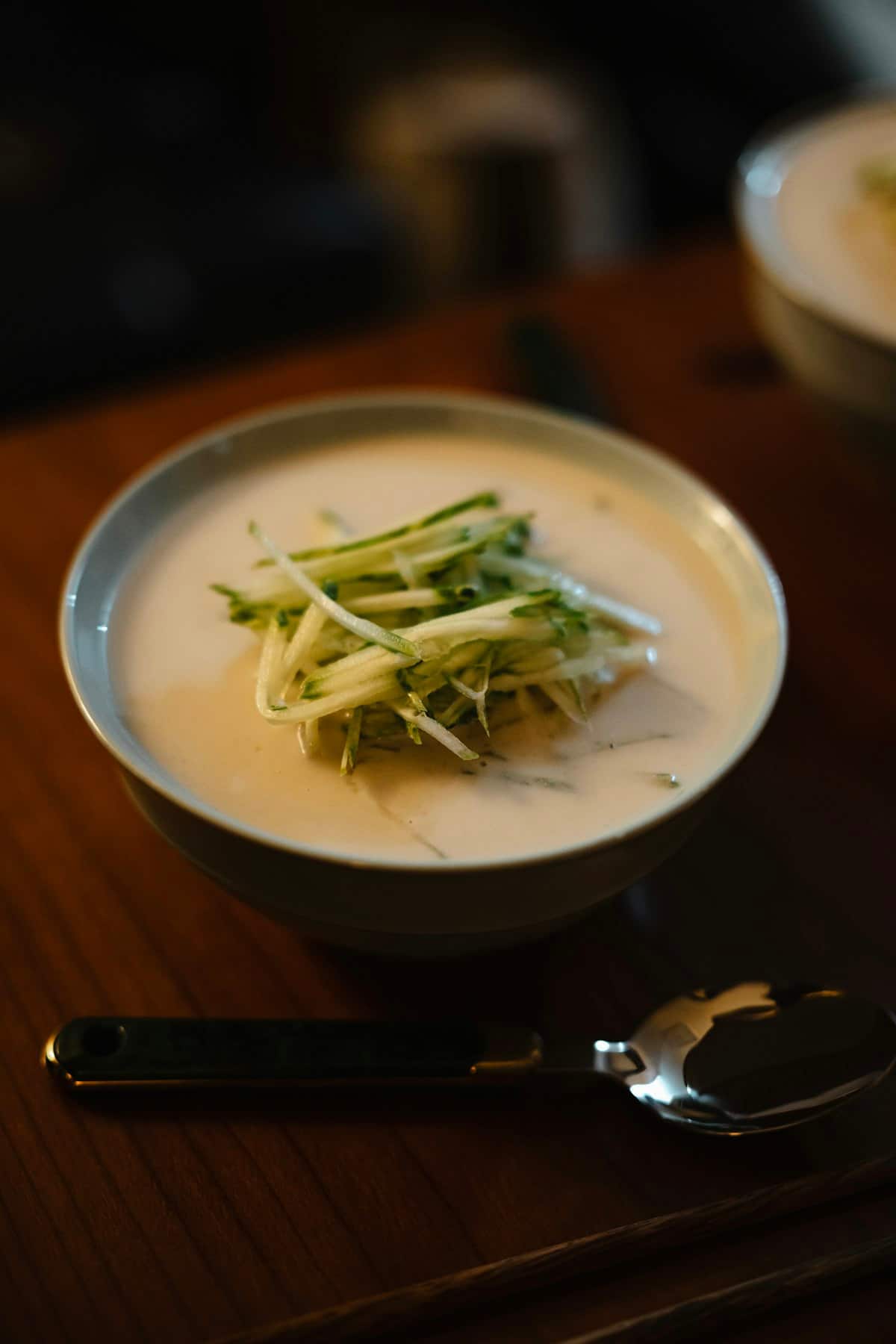 A bowl of pale creamy soup topped with julienned cucumber