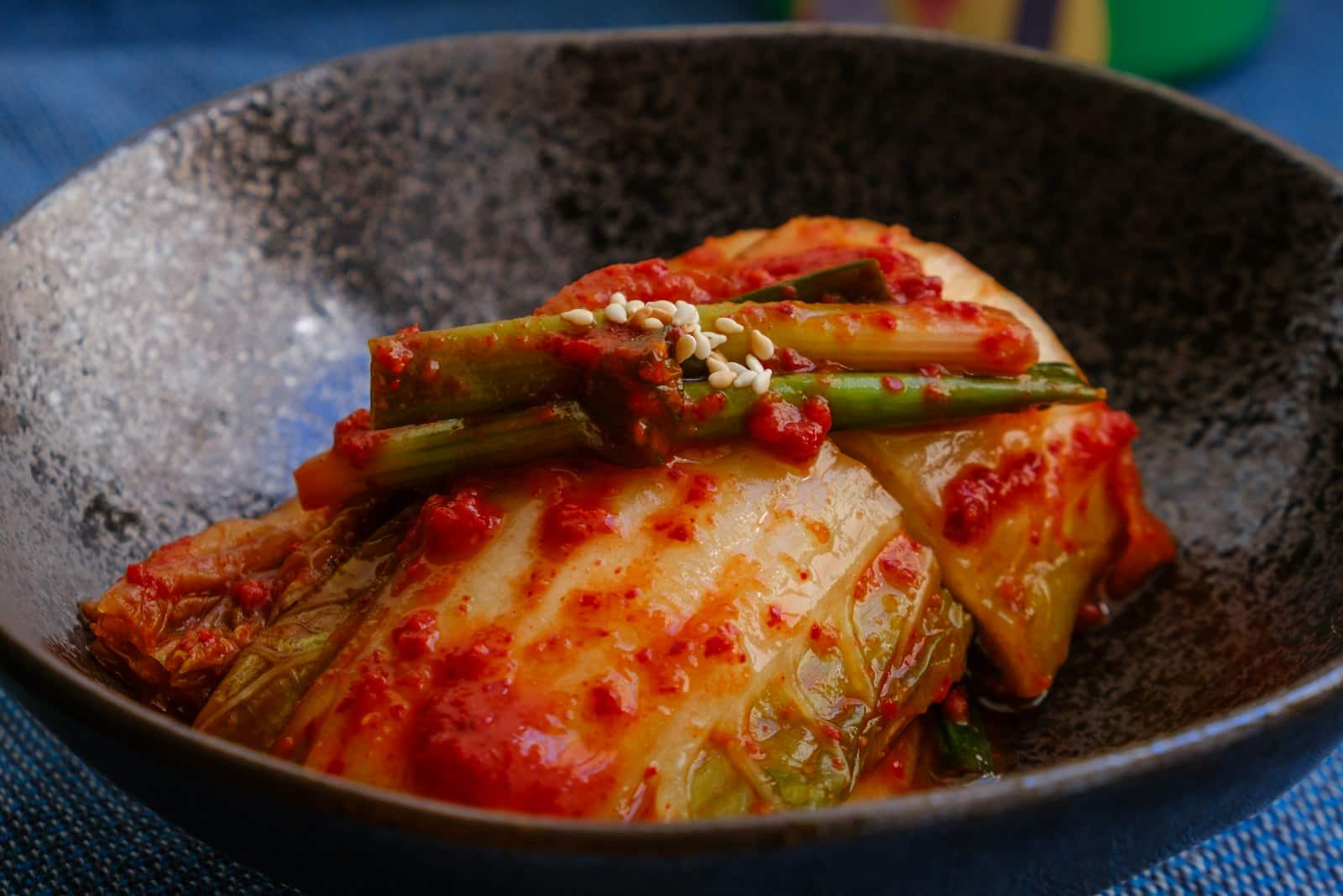 A whole napa cabbage kimchi leaf coated in red chili paste in a rustic bowl