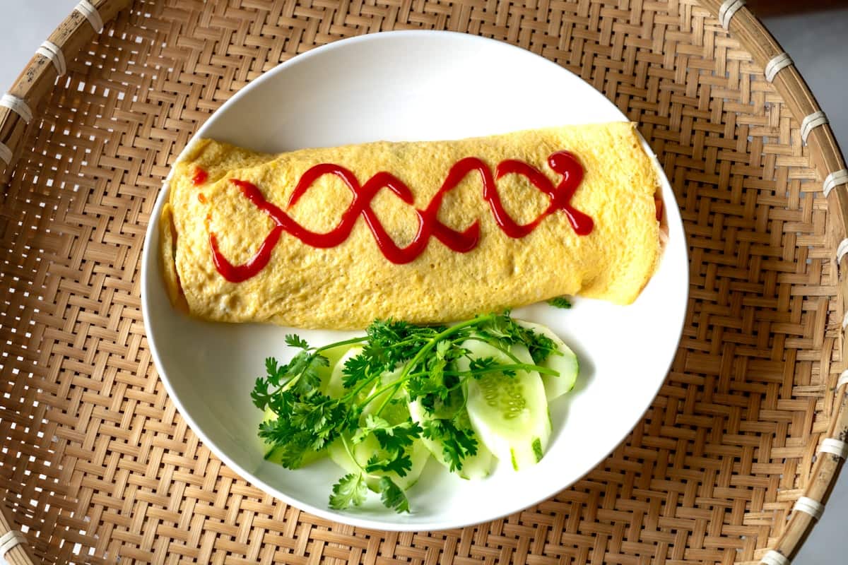 Omelette-wrapped rice topped with a ketchup swirl on a plate