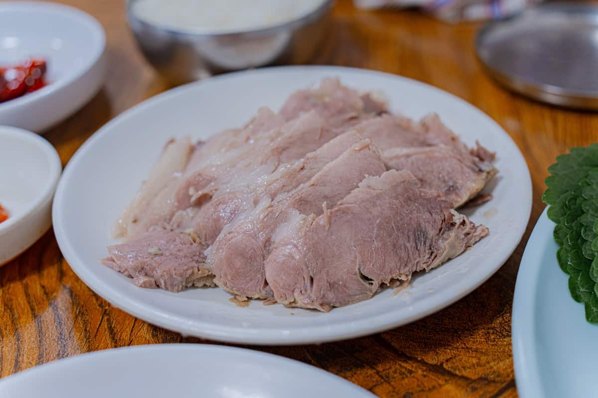 Thin slices of boiled meat arranged on a plate with dipping sauce