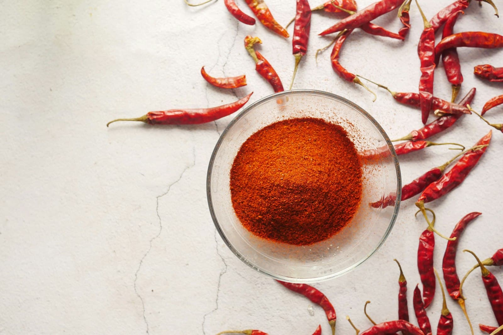 A bowl of red chili powder surrounded by whole dried chilies