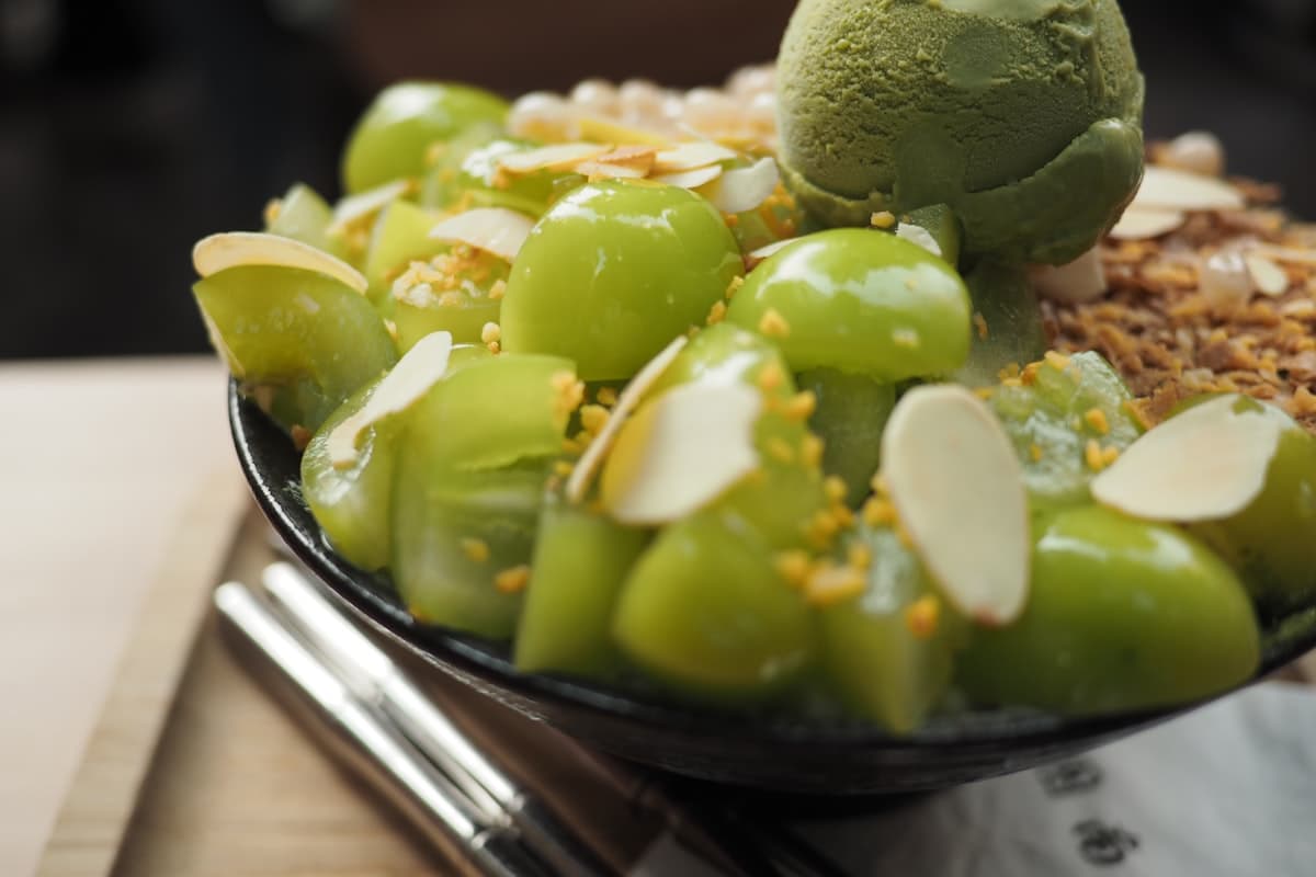 A bowl of melon shaved ice topped with matcha ice cream and almond slices