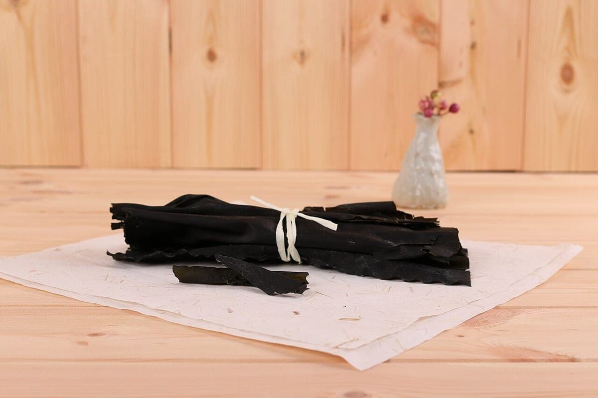 A bundle of dried black kelp tied with string on pale handmade paper