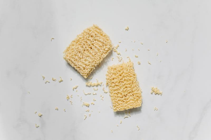 Two dry instant ramen noodle blocks on a marble surface