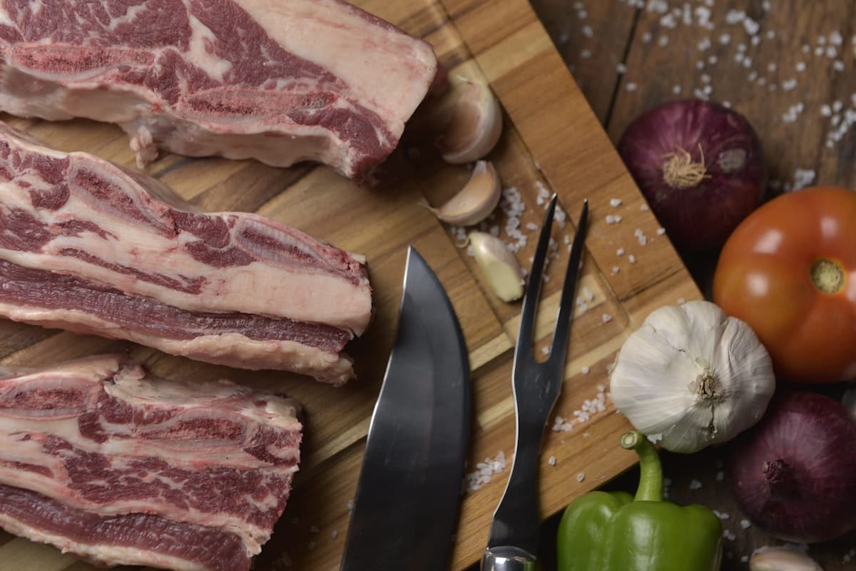 Raw cross-cut short ribs on a wooden cutting board with garlic and vegetables