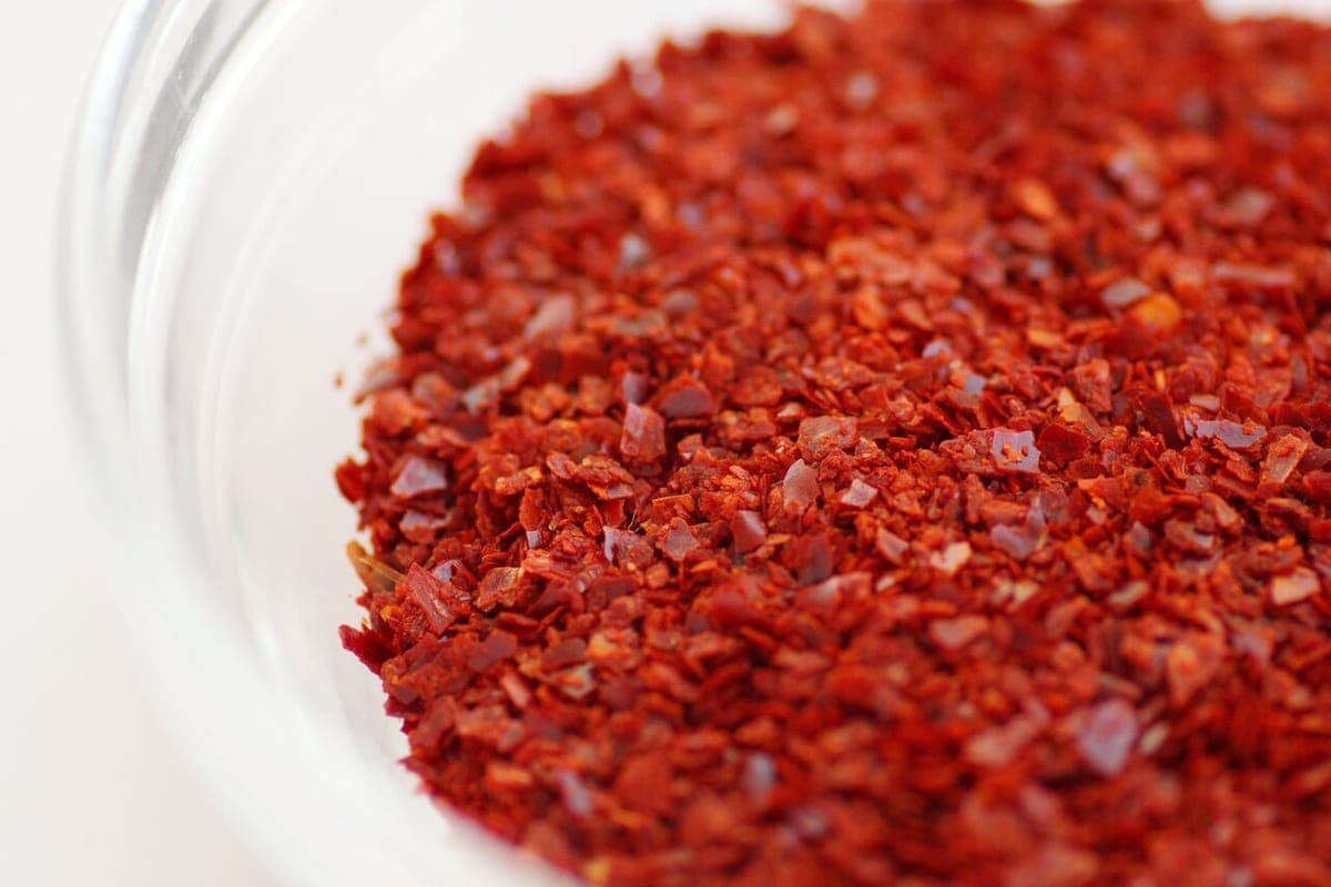 A close-up of coarse red gochugaru flakes in a glass bowl