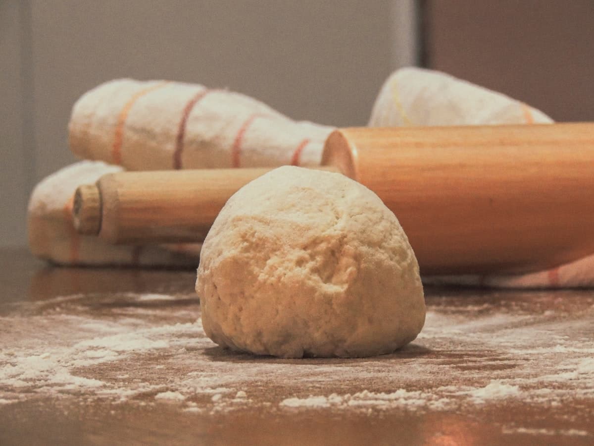 A ball of plain wheat dough next to a wooden rolling pin