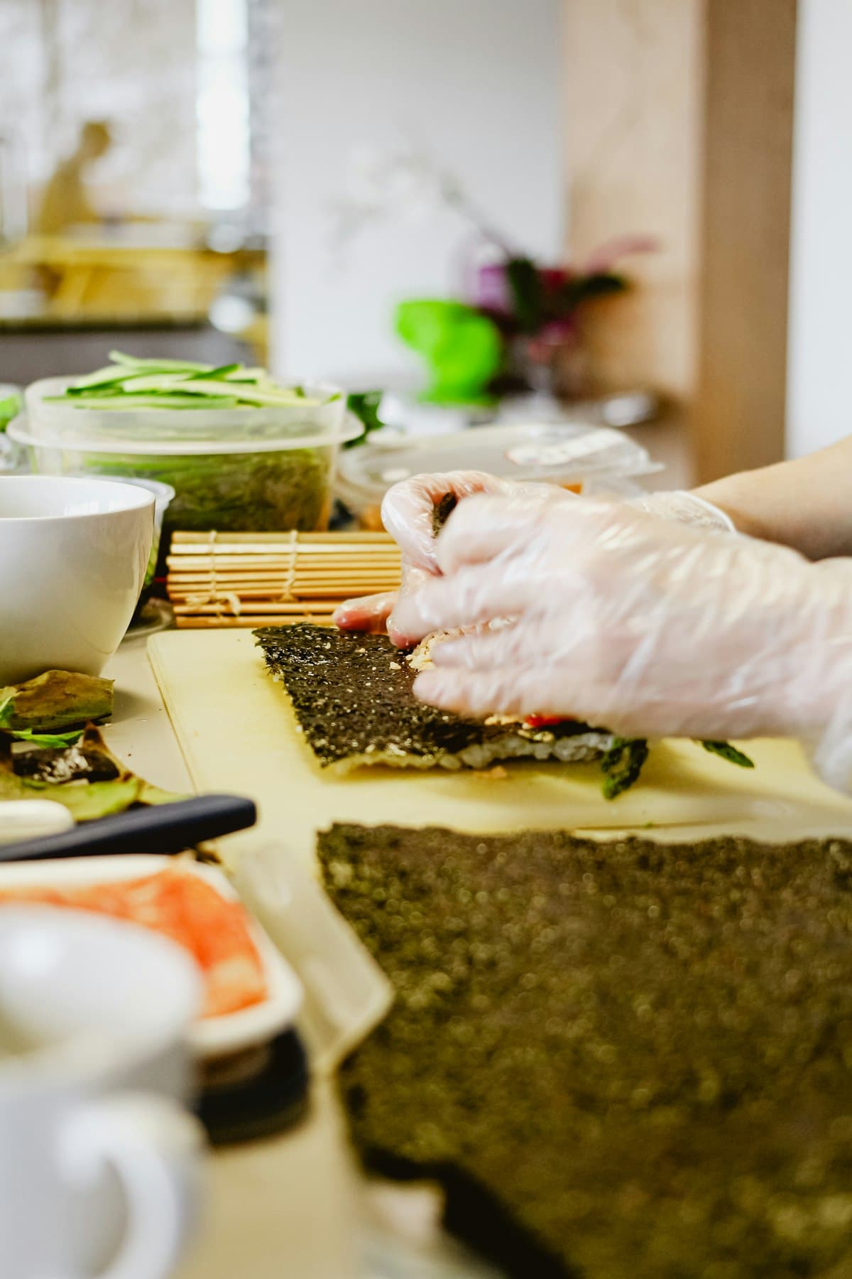 Hands in gloves rolling a seaweed sheet with a bamboo mat