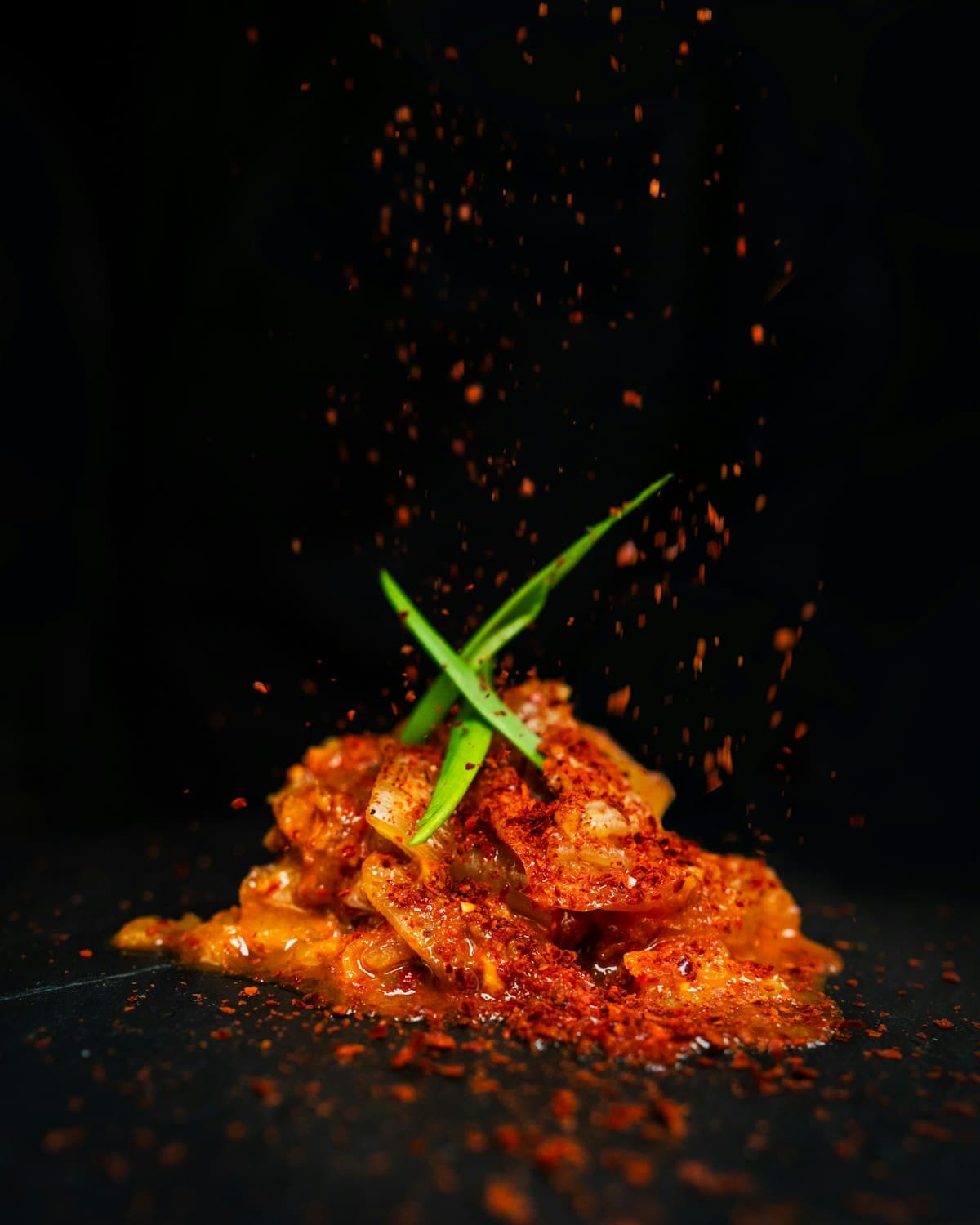 Dramatic close-up of kimchi with gochugaru falling over it against a dark background