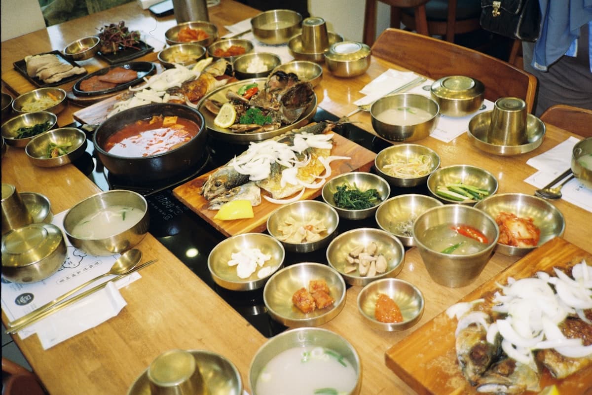 A Korean table crowded with small metal banchan bowls
