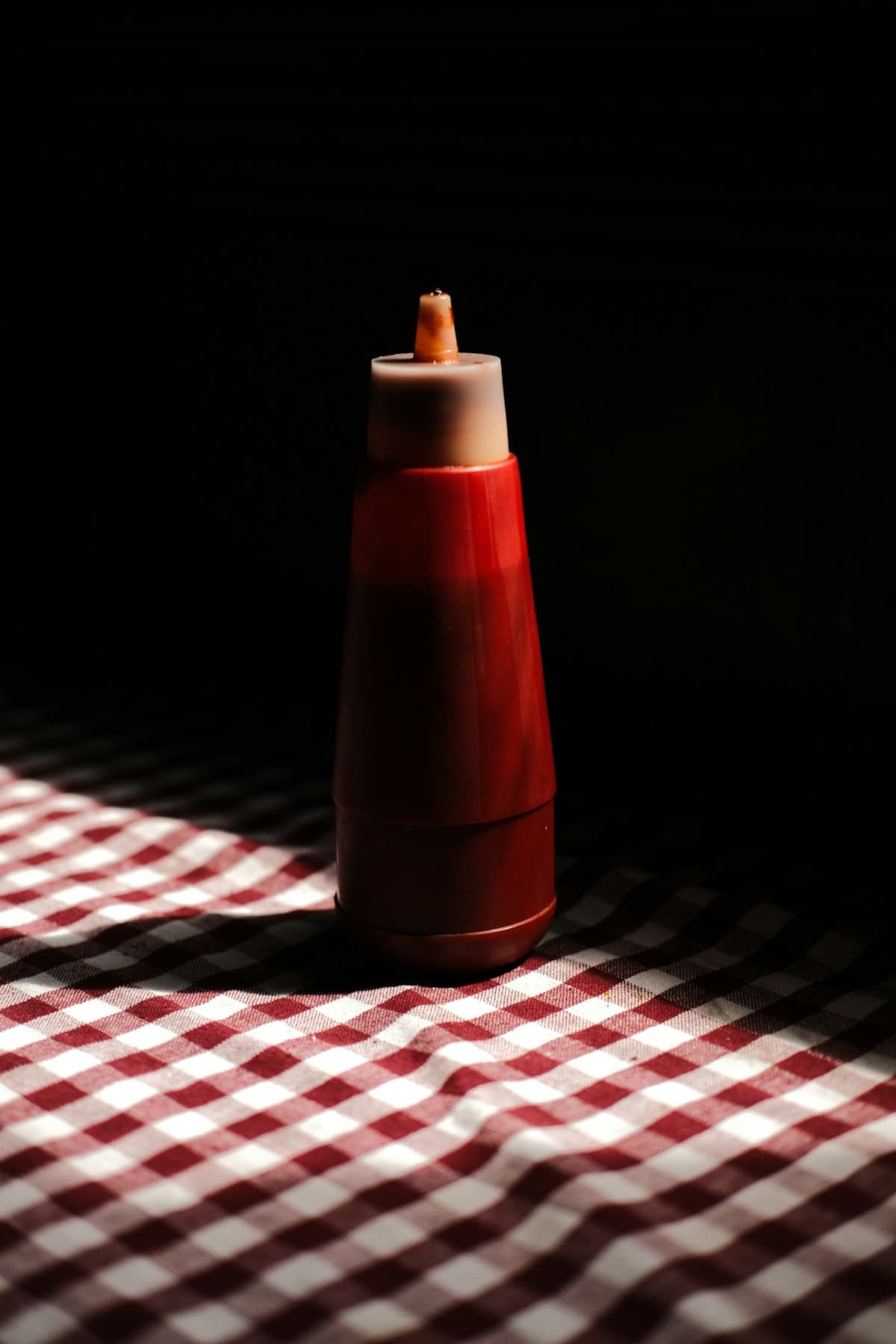 A generic red squeeze bottle on a red-checkered tablecloth
