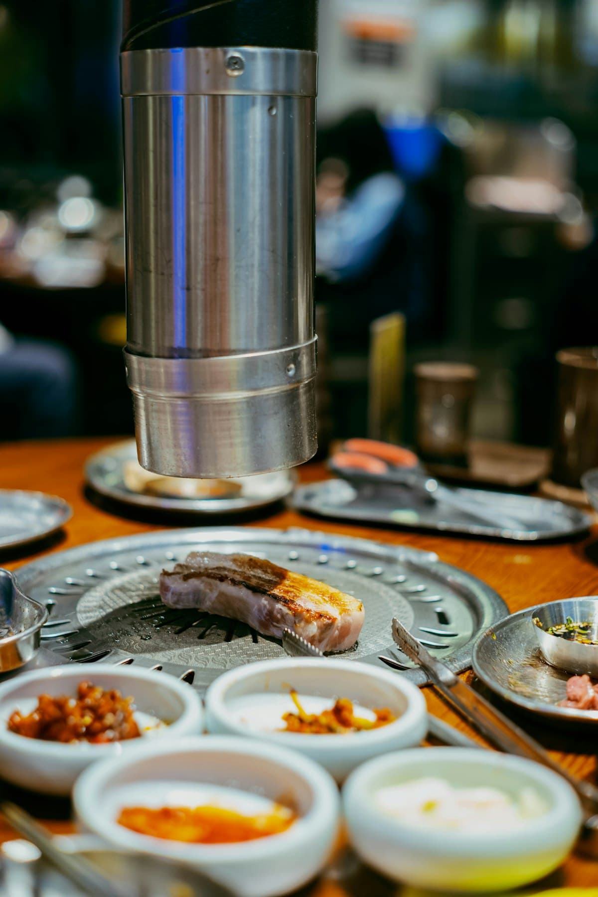 A Korean tabletop grill with meat cooking and side dishes nearby