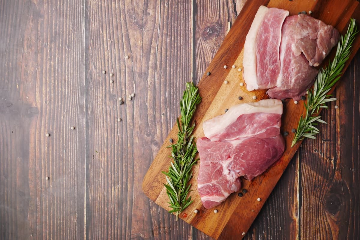 Raw pork cuts on a wooden cutting board with herbs