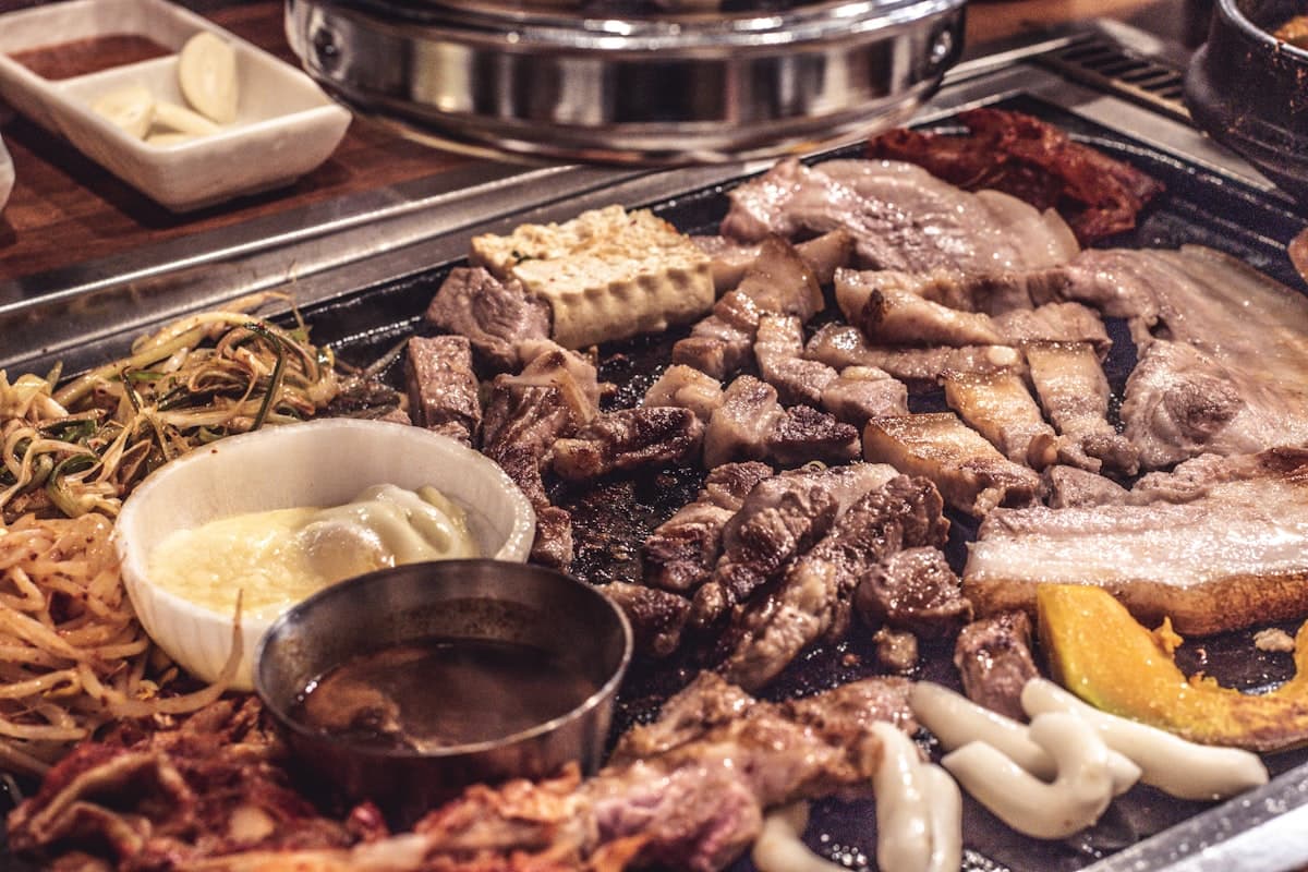 A full spread of Korean BBQ pork belly grilling with side dishes and garlic