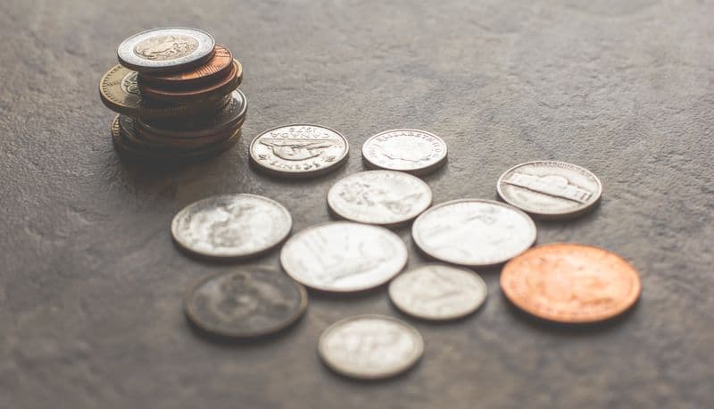 A small stack and scattering of assorted coins on a grey surface