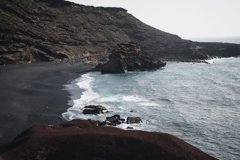 A rocky volcanic coastline with dark sand and cliffs