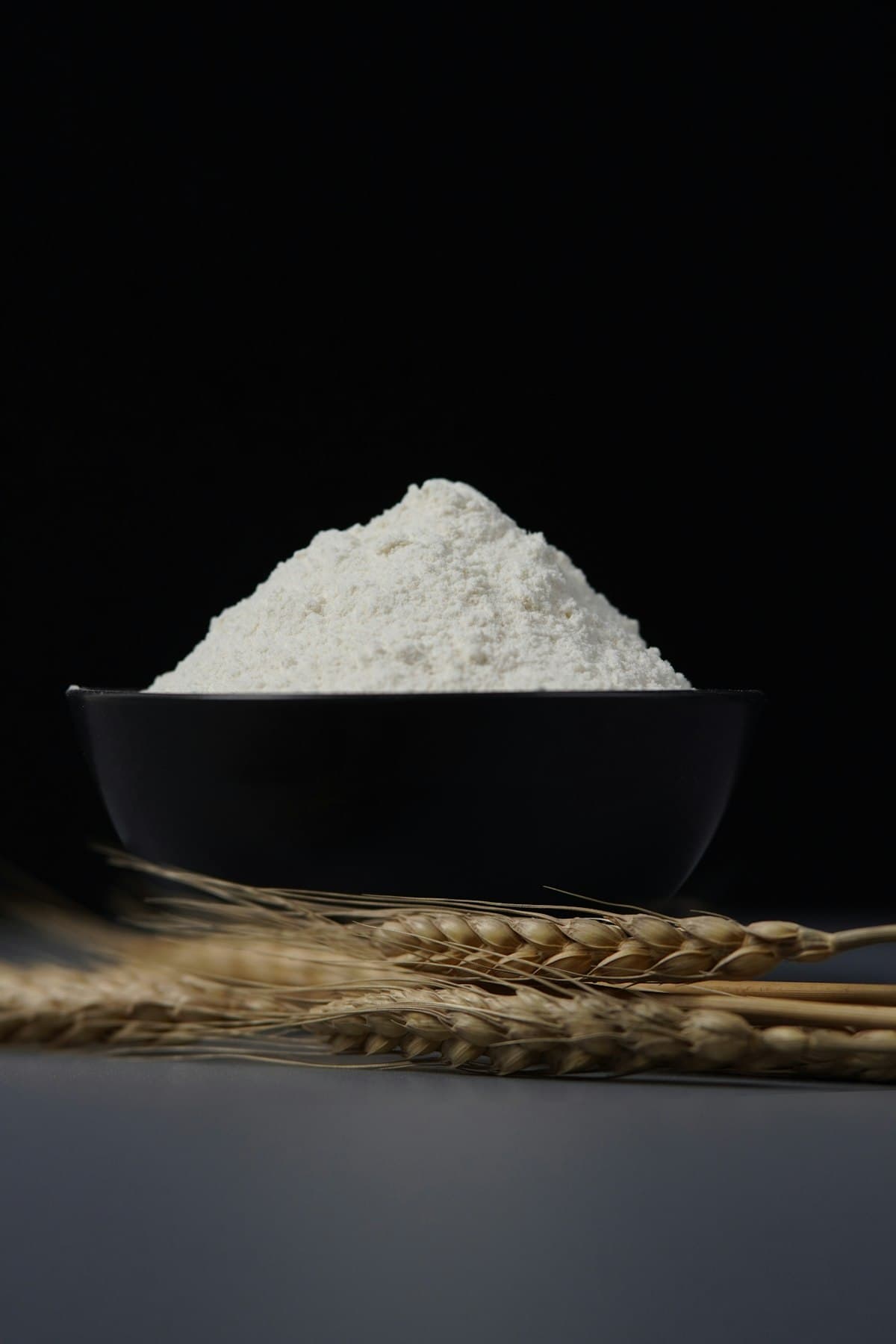 A bowl of white flour beside dried wheat stalks