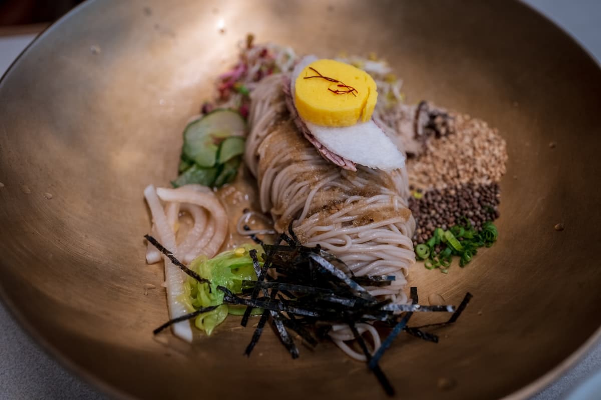A plated cold noodle dish with egg, cucumber, and seaweed garnish
