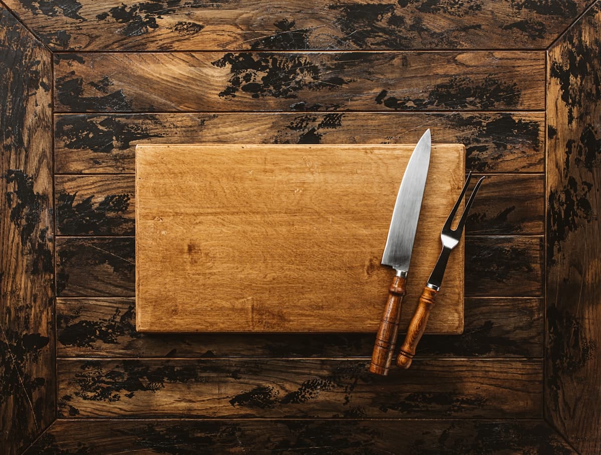 A sharp knife and carving fork resting on a wooden cutting board