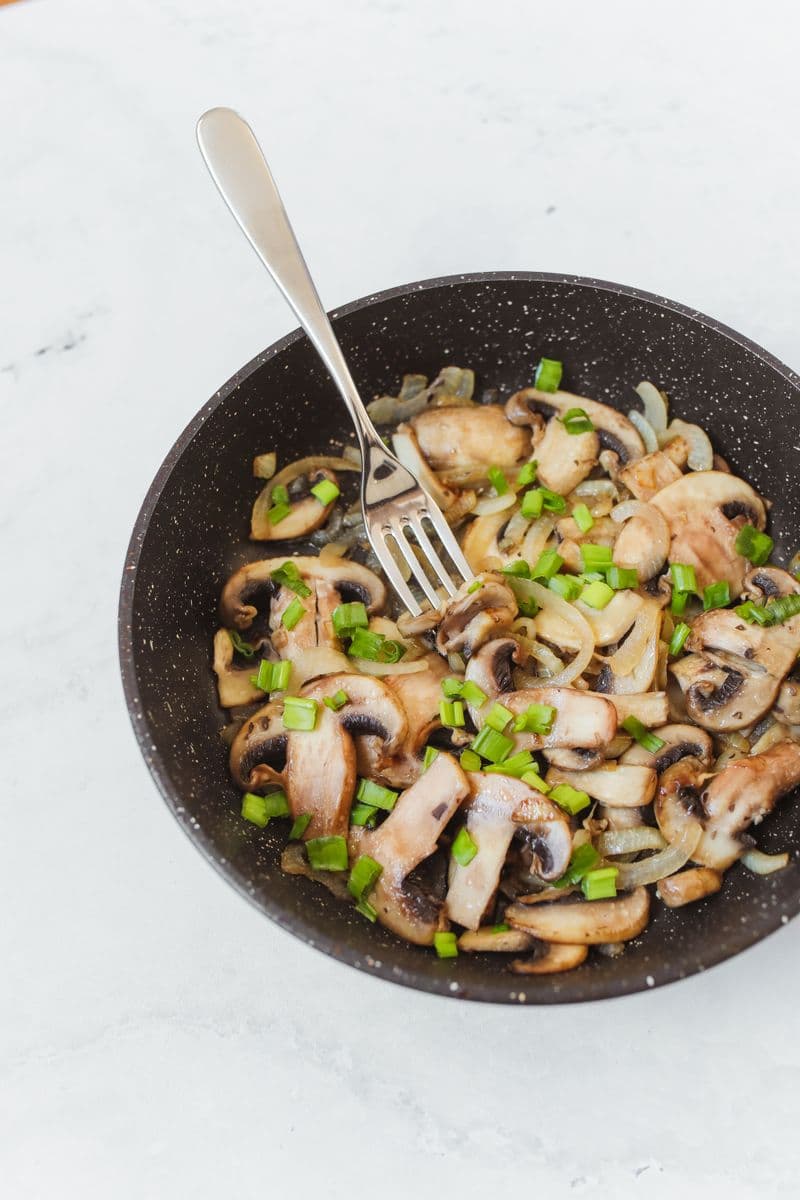 Sauteed mixed mushrooms and onions garnished with green onion in a bowl