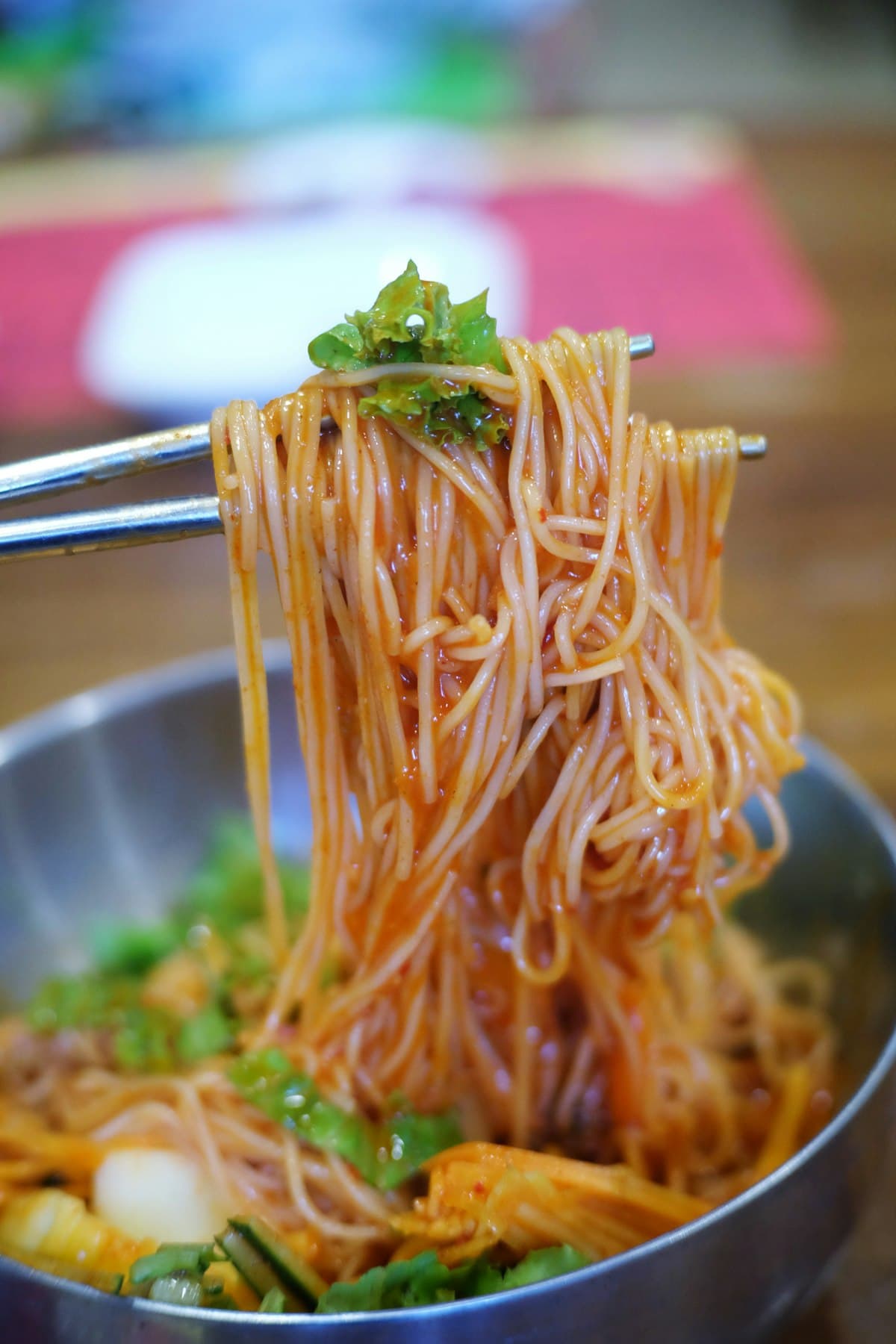 Spicy red-sauced noodles lifted with chopsticks over a metal bowl