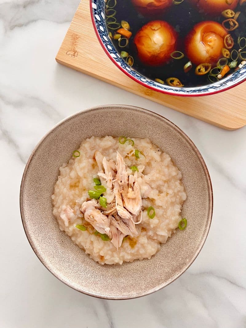 A bowl of creamy chicken rice porridge topped with shredded chicken and scallions