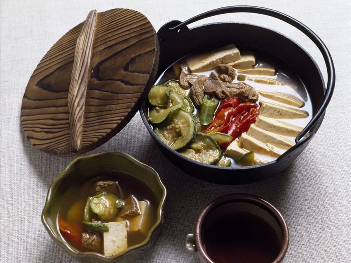 A shallow hot pot of tofu, vegetables and mushrooms arranged in sections
