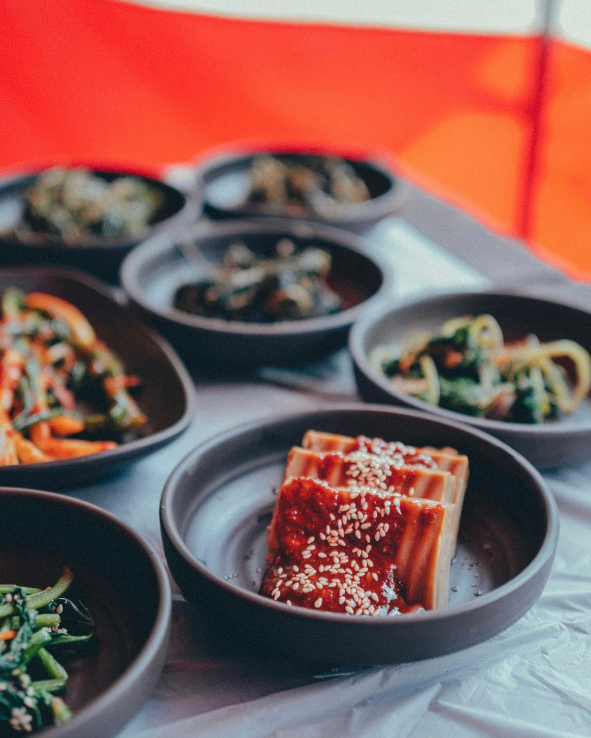 Sliced tofu topped with gochujang sauce next to seasoned banchan