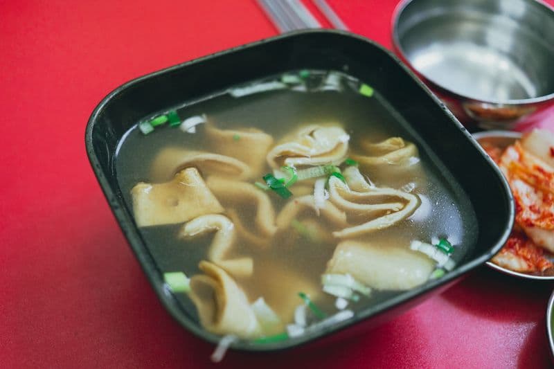Clear broth soup with folded fish cake strips and scallions in a black bowl