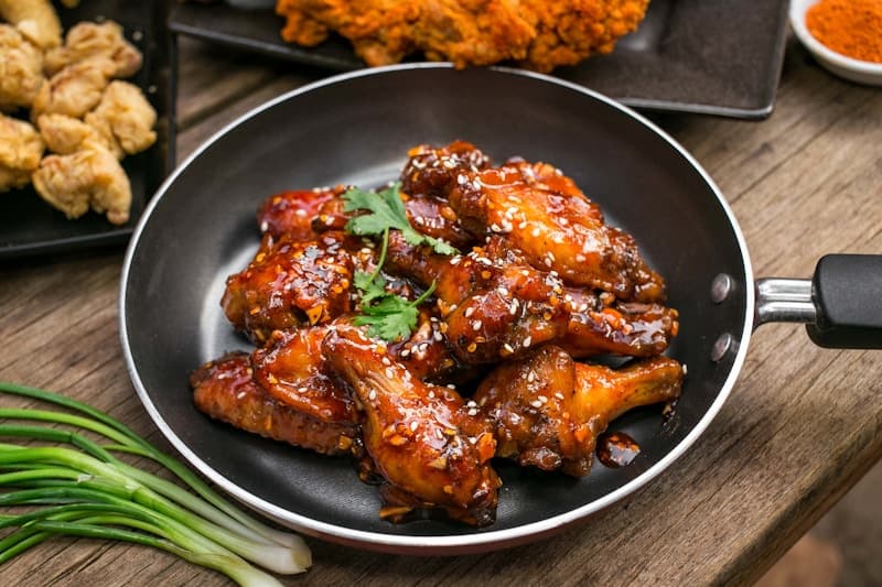 Glossy soy garlic glazed fried chicken wings garnished with sesame seeds in a pan
