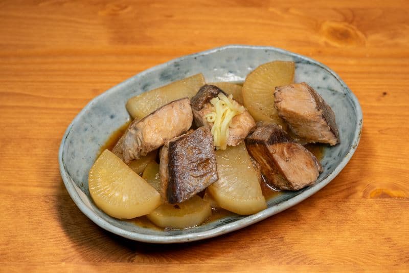 Braised mackerel chunks in dark glaze with daikon radish in a shallow dish