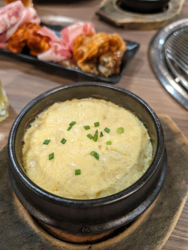 Fluffy domed steamed egg custard in a dark stone bowl, garnished with scallions