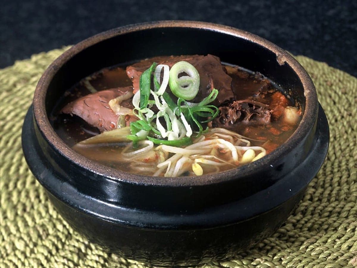 Dark rich soup with bean sprouts and green onion in a stone pot
