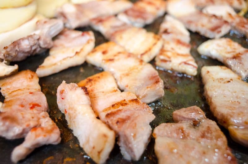 Thick-cut pork belly slices grilling with char marks on a Korean BBQ grill