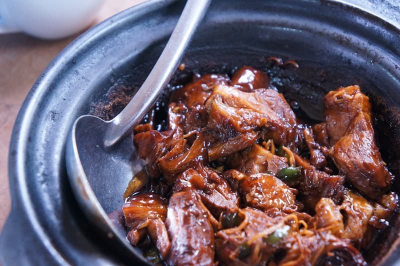Glossy dark braised short ribs in a clay pot with a ladle