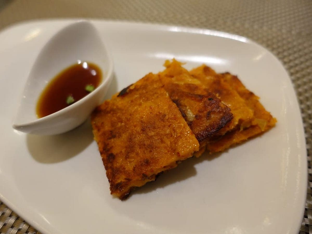 Golden-brown kimchi pancakes on a plate with a small dish of dipping sauce