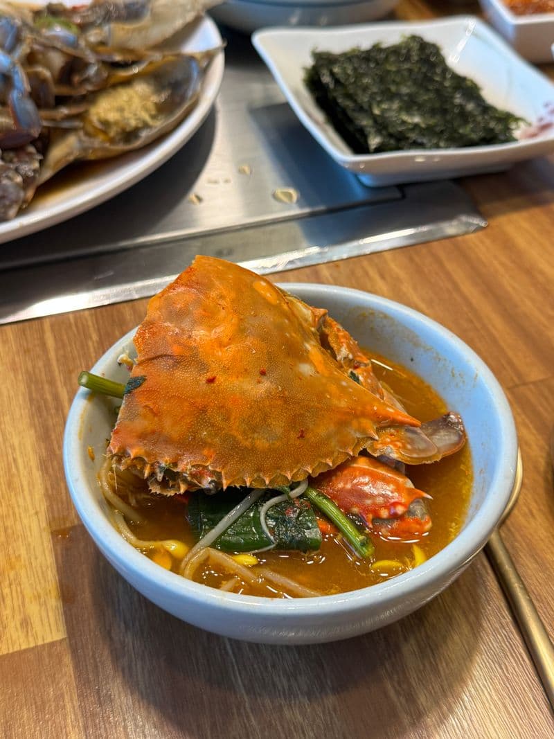 A whole blue crab in spicy red broth with bean sprouts and greens