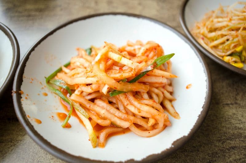 Julienned radish tossed in red seasoning with scallions on a white plate