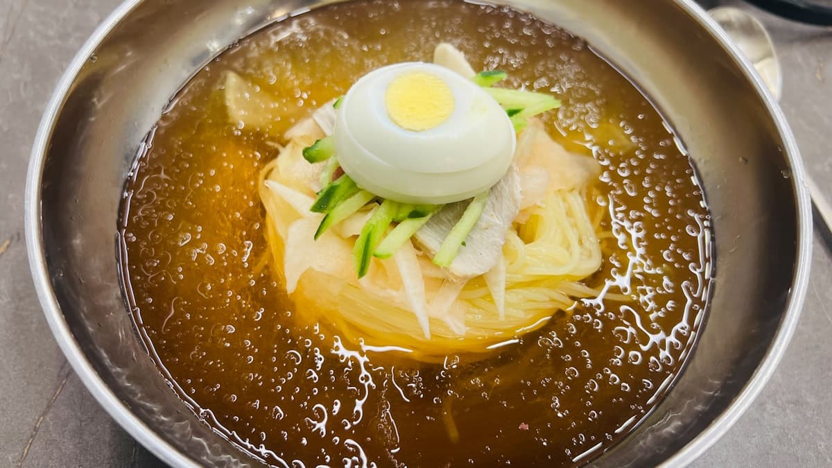 Cold Korean noodles in an icy amber broth topped with egg, cucumber, and radish