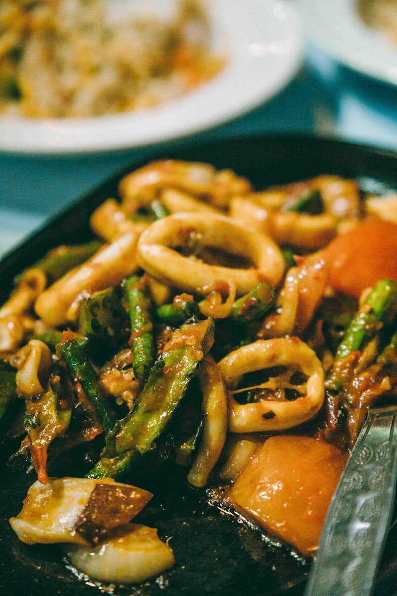 Spicy stir-fried squid rings with vegetables in red sauce on a dark plate