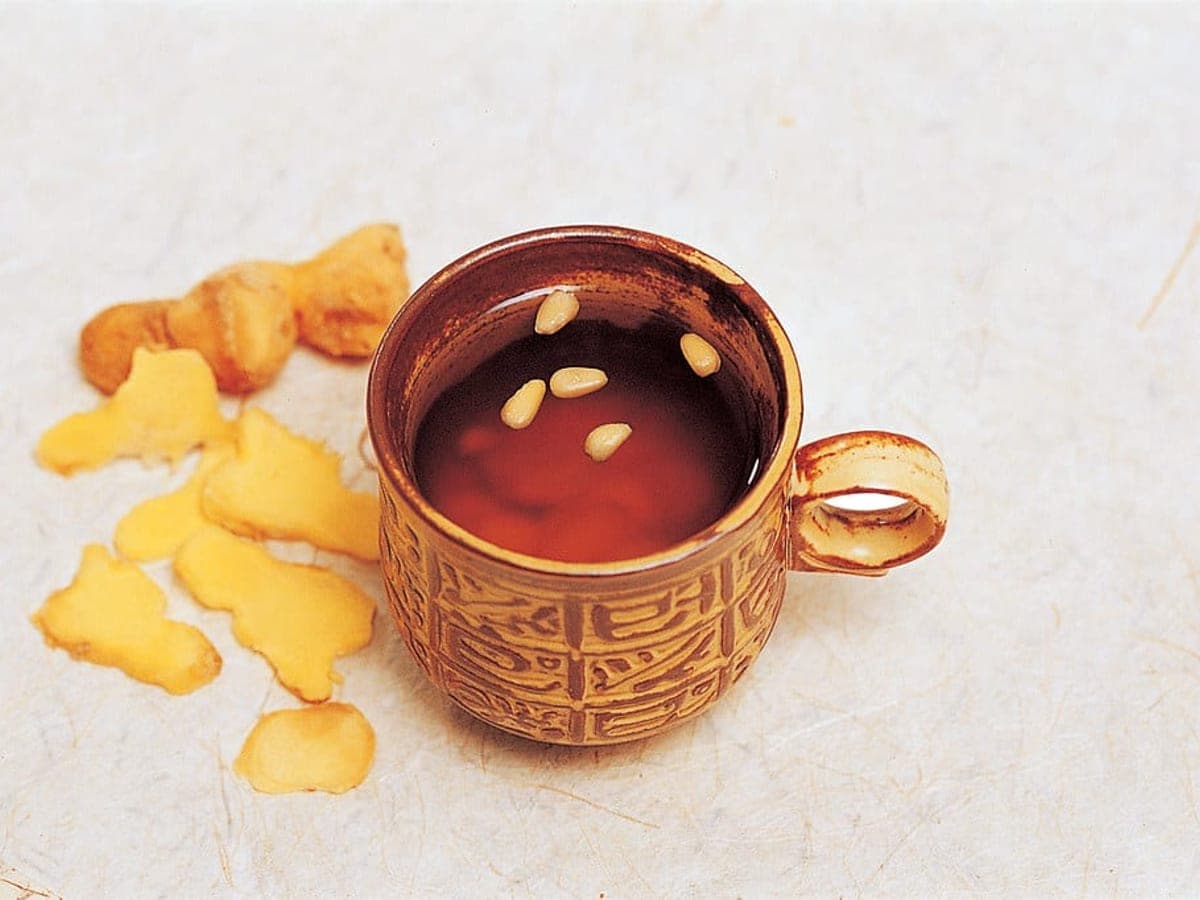 Amber ginger tea in a small cup with pine nuts floating on top