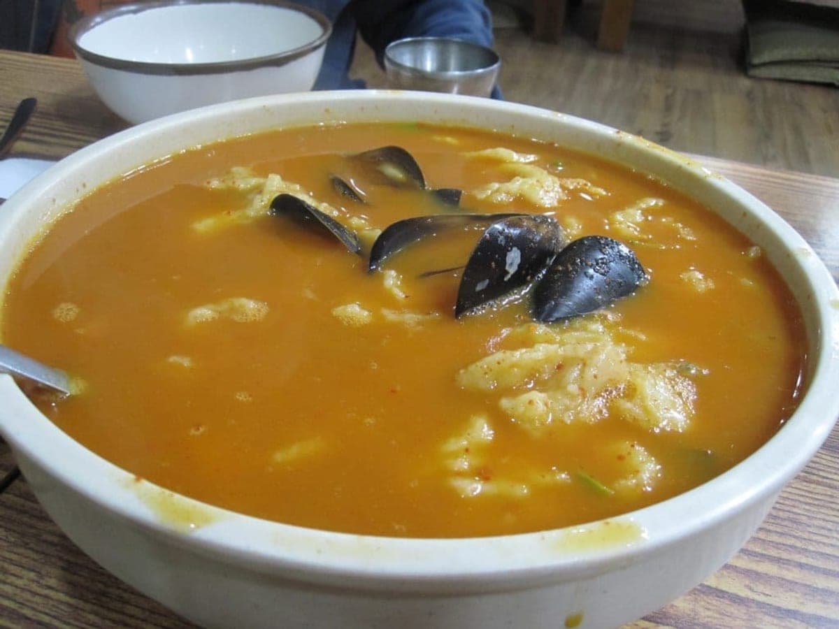 Torn dough pieces and vegetables in a savoury broth in a dark pot